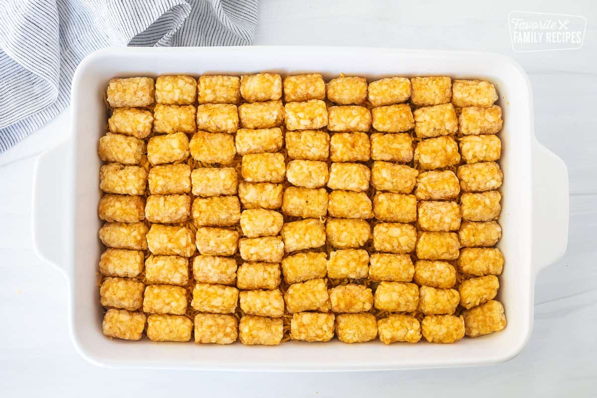 Placing frozen tater tots on top of ground beef mixture casserole and cheddar cheese.