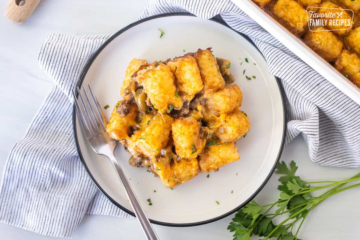 Plate with tater tot casserole dish with ground beef, green beans, cheddar cheese and golden tater tots.