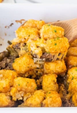 Wooden spoon with tater tot casserole dish with ground beef, green beans, cheddar cheese and golden tater tots.