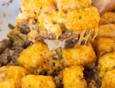 Wooden spoon with tater tot casserole dish with ground beef, green beans, cheddar cheese and golden tater tots.