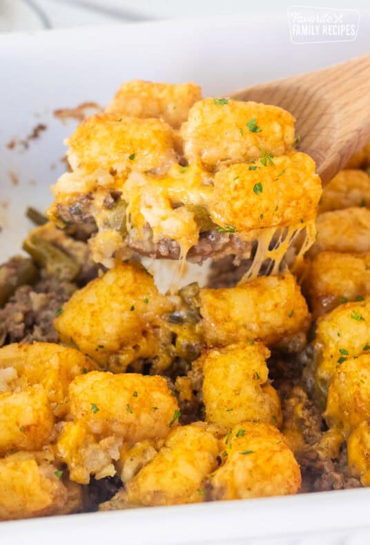 Wooden spoon with tater tot casserole dish with ground beef, green beans, cheddar cheese and golden tater tots.