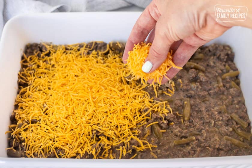Sprinkling cheddar cheese on top of ground beef casserole mixture.