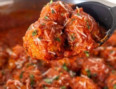 Turkey meatballs in a skillet with sauce being lifted with a serving spoon