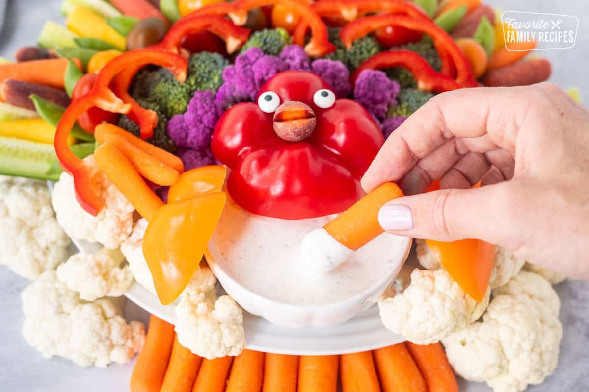 Dipping a baby carrot into bowl of Ranch dip on a turkey shaped veggie tray.