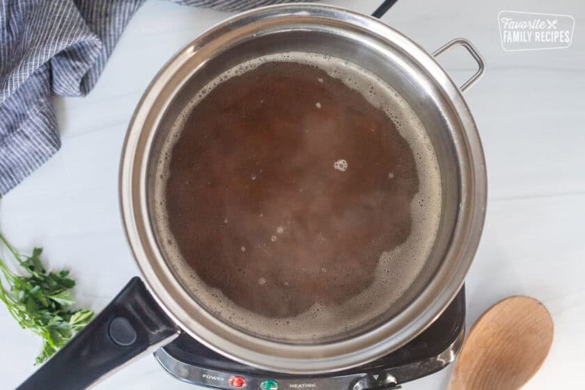 Sauce pan with wild rice, chicken stock and butter simmering on an electric skillet.
