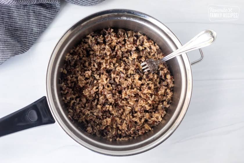 Sauce pan with cooked wild rice fluffed with a fork.