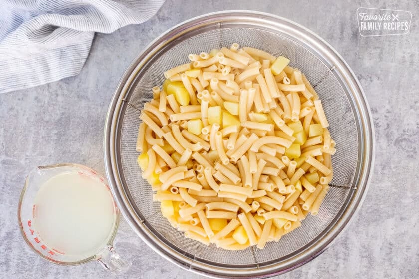Colander with cooked pasta and potatoes with pasta water on the side.