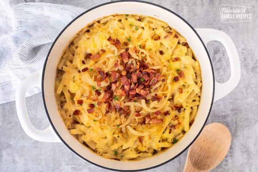 Baked Alplermagronen in a dutch oven topped with caramelized onions and bacon.
