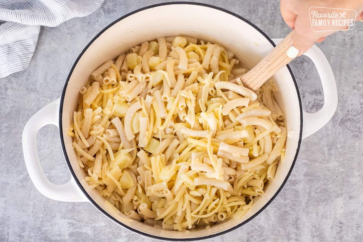 Stirring in the shredded cheese to Alplermagronen in dutch oven.