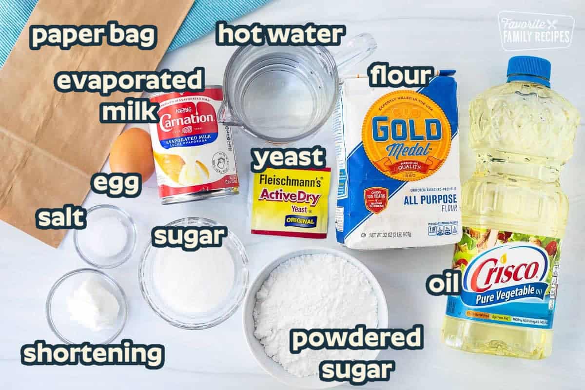 Ingredients to make New Orleans style beignets including oil, flour, water, evaporated milk, paper bag, egg, salt, Crisco shortening, powdered sugar, sugar and yeast.
