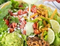 Creamy green dressing poured over a pulled pork taco salad with lettuce, tomatoes, guacamole, cheese, and tortilla strips.