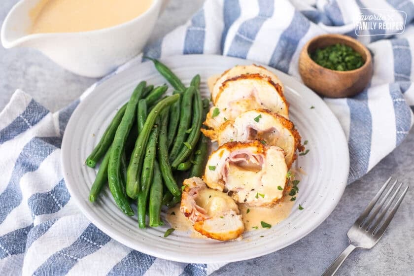 Plate with sliced chicken cordon bleu with sauce and green beans on the side.