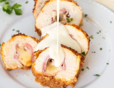 Pouring chicken Cordon Bleu Sauce from a saucer onto sliced chicken cordon bleu.