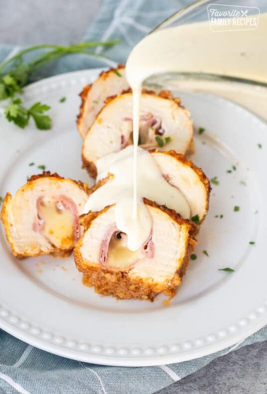 Pouring chicken Cordon Bleu Sauce from a saucer onto sliced chicken cordon bleu.