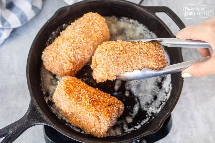 Placing an uncooked chicken cordon bleu into a hot skillet with melted butter.