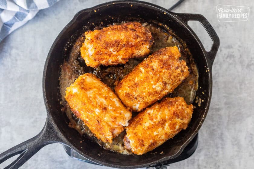 Four golden pieces of chicken cordon bleu in a skillet.