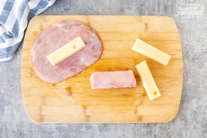 Cutting board with ham rolled around Swiss cheese stick.