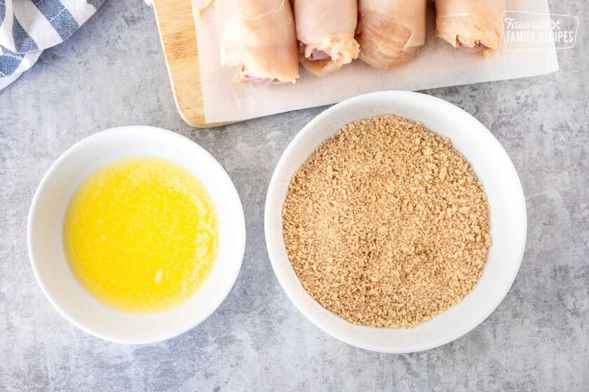 Rolled up chicken cordon bleu next to a bowl of melted butter and bowl of panko mixture.