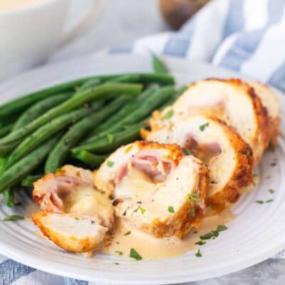 Sliced chicken cordon bleu with sauce and green beans on the side.