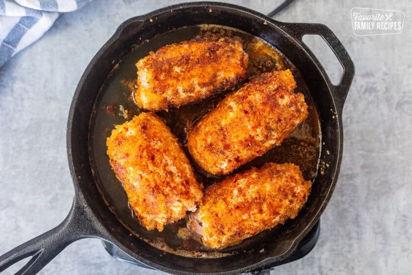 Chicken broth in a skillet of four pieces of chicken cordon bleu.
