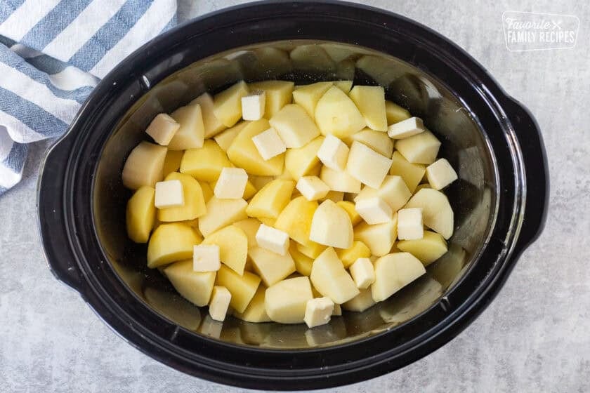 Potato chunks in a slow cooker with chicken broth, butter, and salt.