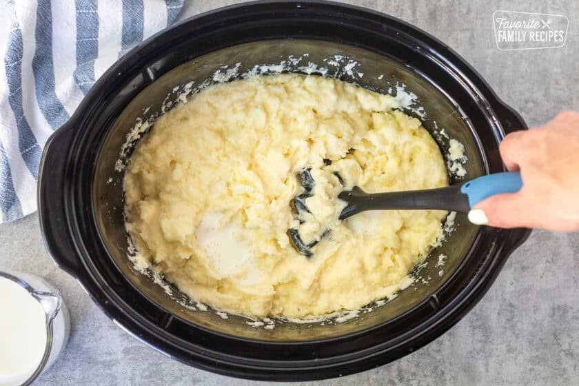 Combining milk with the mashed potatoes in a crockpot with a potato masher.