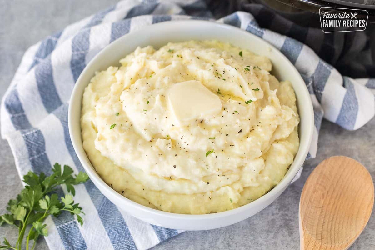 Bowl of crockpot of mashed potatoes with a pad of butter.