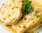 Pork chops in creamy gravy served over mashed potatoes and garnished with fresh parsley on a white plate.