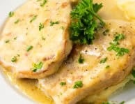 Pork chops in creamy gravy served over mashed potatoes and garnished with fresh parsley on a white plate.