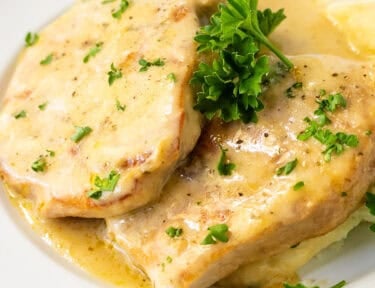 Pork chops in creamy gravy served over mashed potatoes and garnished with fresh parsley on a white plate.