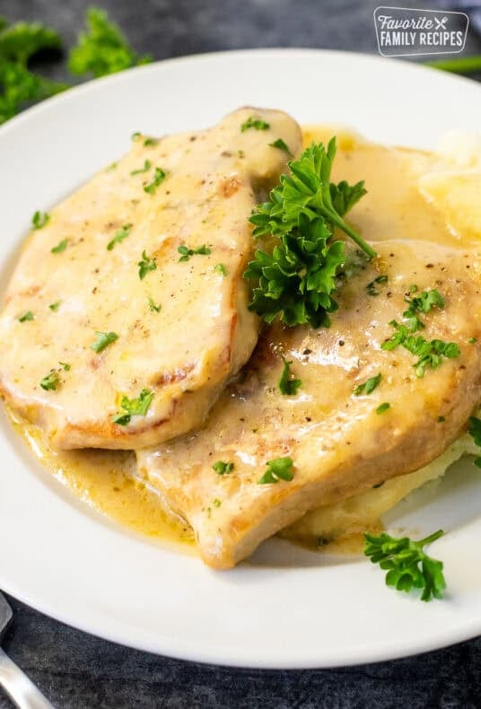 Pork chops in creamy gravy served over mashed potatoes and garnished with fresh parsley on a white plate.