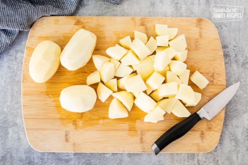 Cutting board with peeled and cut potatoes with a knife.