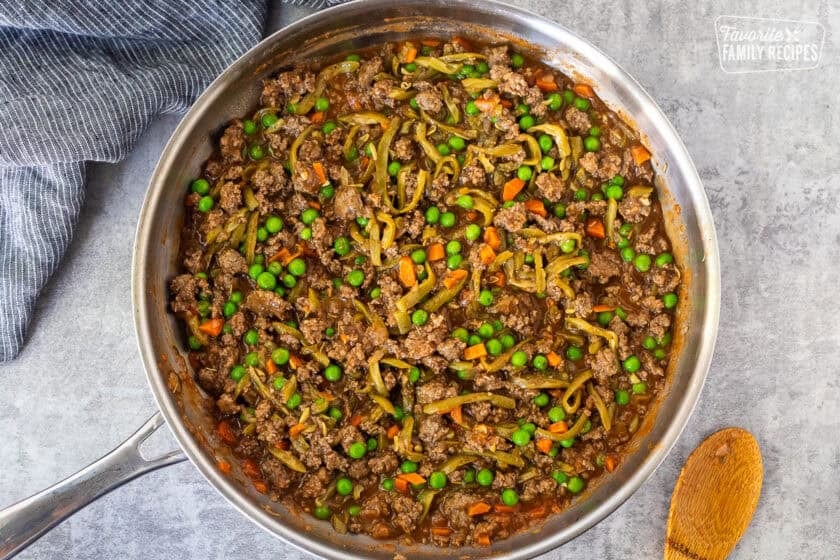 Shepherds pie filling in a skillet including ground beef, tomato sauce, French style green beans, peas, carrots and onion.