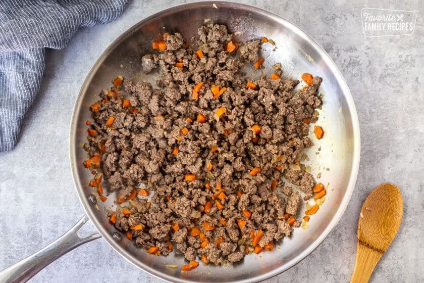 Skillet with browned ground beef and carrots and onions.