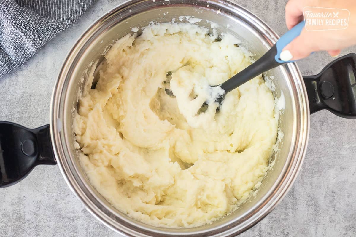 Mashing up potatoes in a large pot with a potato masher.
