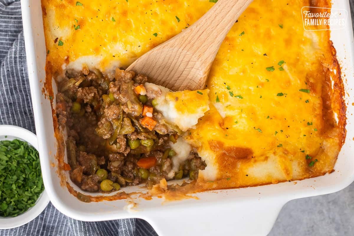 Easy shepherds pie with a wooden spoon scooping a portion from the casserole dish.