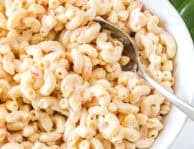 Creamy macaroni salad with elbow pasta and shredded carrots in a white bowl with a serving spoon.