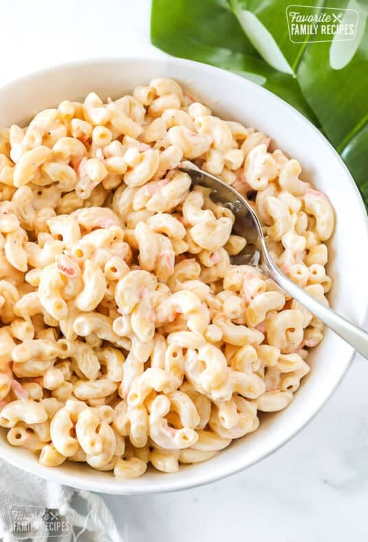 Creamy macaroni salad with elbow pasta and shredded carrots in a white bowl with a serving spoon.