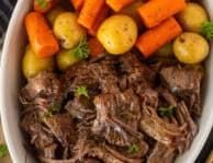 Instant Pot chuck roast with shredded beef, baby potatoes, and carrots, garnished with parsley on a white serving platter.