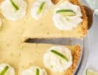 Key lime pie with a graham cracker crust, whipped cream, and lime slices, with one slice lifted on a pie server.