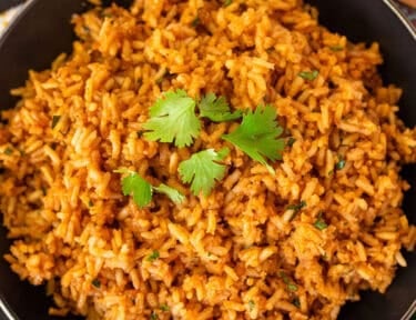 Mexican rice garnished with fresh cilantro in a black skillet, with tortilla chips and pico de gallo alongside.