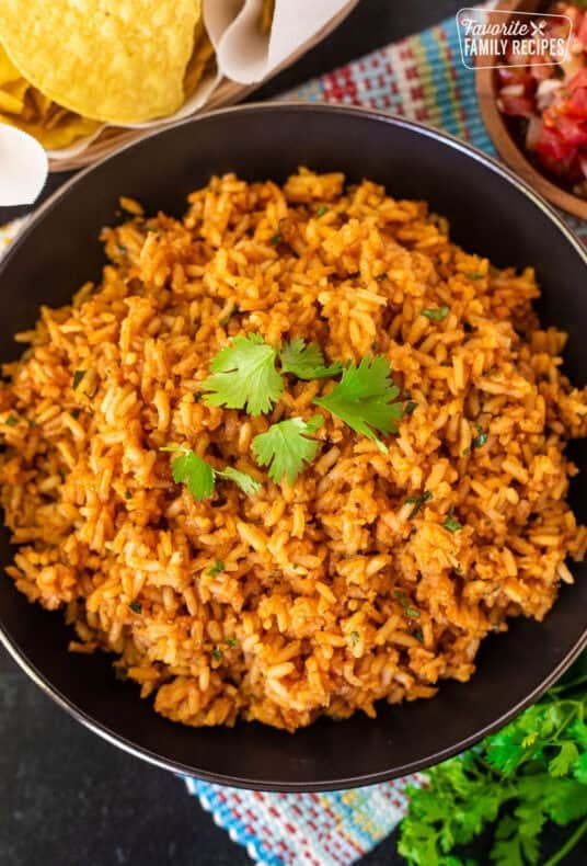 Mexican rice garnished with fresh cilantro in a black skillet, with tortilla chips and pico de gallo alongside.