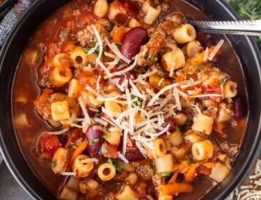 Olive Garden pasta fagioli soup with ground beef, beans, ditalini pasta, and vegetables, topped with Parmesan in a black bowl.