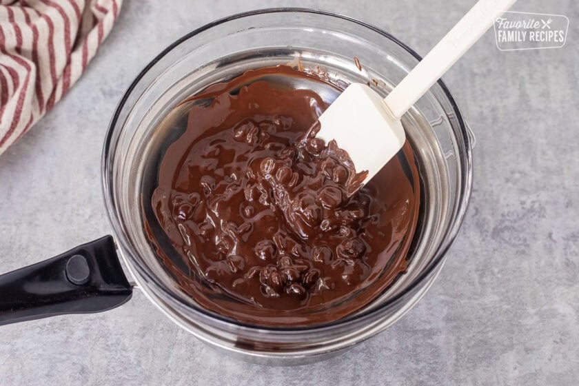 Melting dark chocolate in a bowl over saucepan and stirring with a spatula.