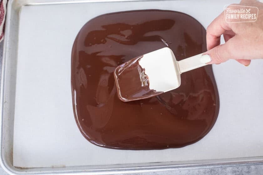Spreading out melted dark chocolate on parchment paper.