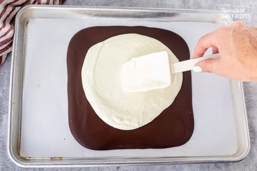 Spreading peppermint white chocolate over cooled dark chocolate with a spatula.