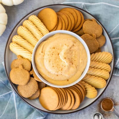 Plate with a center bowl of pumpkin dip surrounded by ginger pumpkin cookies, vanilla wafers and ginger snaps.