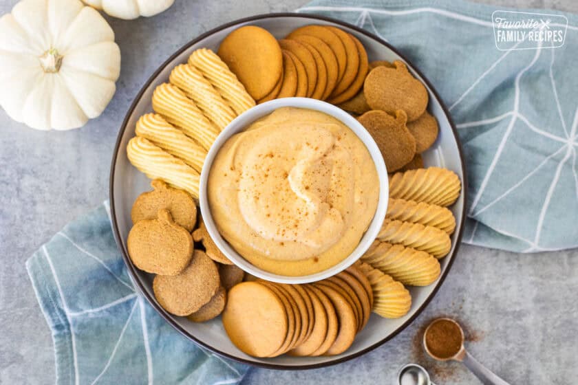 Plate with a center bowl of pumpkin dip surrounded by ginger pumpkin cookies, vanilla wafers and ginger snaps.
