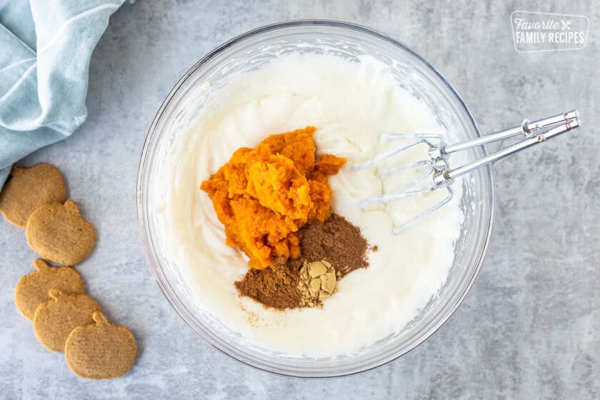 Glass mixing bowl with cream cheese base, pumpkin and spices. Electric beaters resting in the bowl.