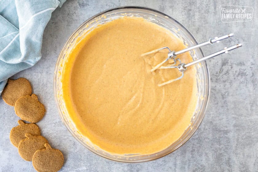 Pumpkin dip in a glass mixing bowl with electric beaters resting on the side of the bowl.